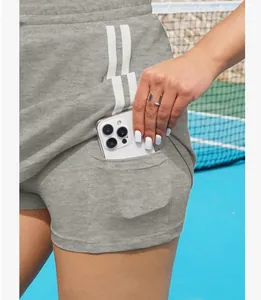 Detail van grijze tennisrok met handige zijzak voor telefoon en witte zijstrepen.