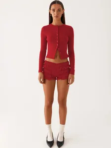 Woman wearing a red slim-fit ribbed cardigan and matching ruffled shorts in a studio