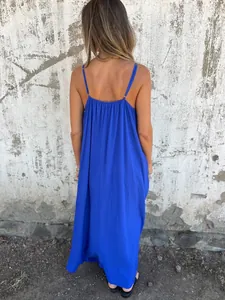 Back view of a vibrant royal blue spaghetti strap maxi dress against a rustic wall