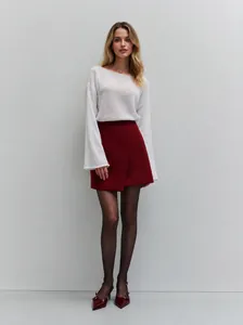 Elegante minifalda cruzada roja de cintura alta con un suéter blanco y medias negras en modelo