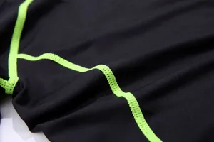 Macro view of black quick-dry athletic fabric featuring vibrant green flatlock seams.