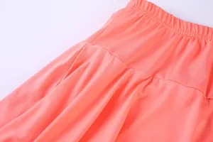 Close-up detail showing the elastic waistband and pleated texture of a coral tennis skort