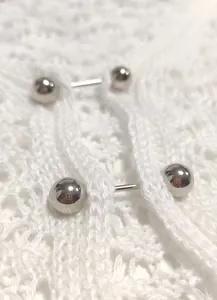 Macro detail of white crochet beach cover-up featuring a silver metal barbell closure