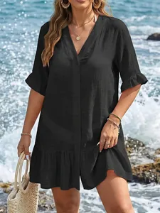 Detalle de un vestido de playa negro con escote en V, volantes y botones frente al mar.