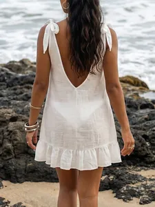 Back view of white beach cover-up dress with V-neck and bow straps on a rocky beach shore