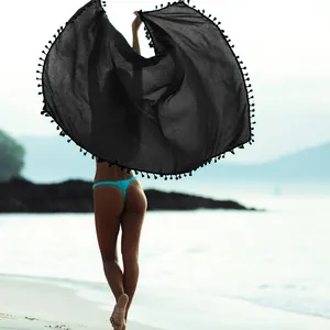 Azione di una modella che tiene un grande scialle da spiaggia nero con nappe in spiaggia
