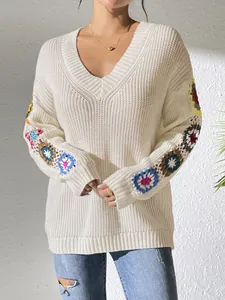 Détail d'un pull en maille blanc à col en V avec des fleurs au crochet sur les manches