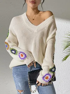 Détail d'un pull en tricot blanc à col en V avec des fleurs colorées au crochet sur les manches