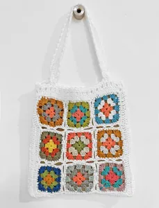 Vista dettagliata di una borsa tote colorata fatta a mano all'uncinetto su una parete bianca.