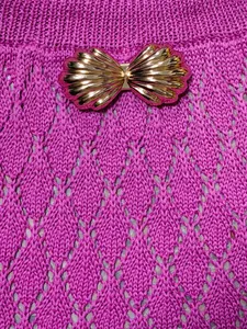Détail macro de robe en maille ajourée rose avec boucle dorée en forme de coquille.