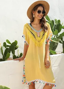 Model wearing yellow crochet beach cover-up with colorful tassels in outdoor setting.
