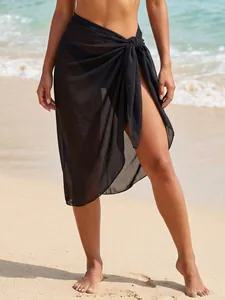 Close-up of a black sheer chiffon sarong wrap tied at the waist on a sunny sandy beach