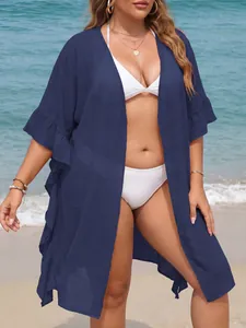 Plus size navy blue ruffled cover up cardigan shown over a white bikini on a sunny beach.