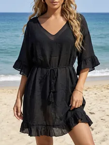 Elegante vestido de playa negro con cuello en V, mangas con volantes y borlas en la playa.