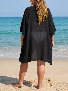 Back view of a loose black plus size beach cover-up with textured fabric on a sandy beach