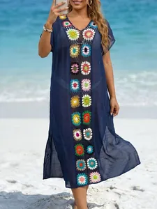 Lange marineblauwe strandcover-up met kleurrijke gehaakte bloemen op een zonnig strand