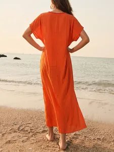Achteraanzicht van een levendige oranje strand maxi-jurk op een prachtig zandstrand