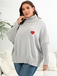 Close-up view of gray oversized turtleneck knit sweater featuring a red heart patch