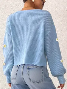 Detail einer hellblauen Strickjacke mit weißen Häkelblumen-Aufnähern an Ärmeln