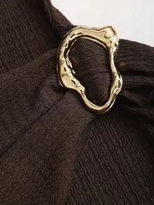 Macro detail showing an irregular gold metal buckle on a dark brown textured knit dress.