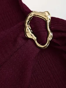 Close-up of knitted textured fabric and irregular gold buckle on a wine red dress