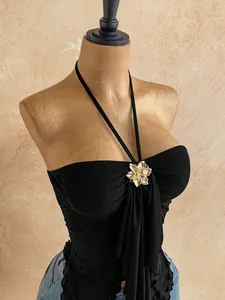 Detail of black double-layer mesh halter tube top with gold flower and irregular hem.