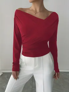 Dettaglio della maglia rossa a maniche lunghe con scollo a barca e elegante drappeggio.