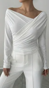 Dettaglio dell'elegante trama a pieghe del top bianco a maniche lunghe con spalle scoperte
