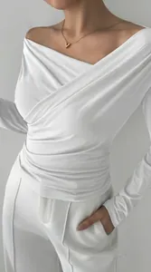Dettaglio top bianco a maniche lunghe con spalle scoperte e design drappeggiato