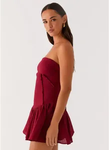 Side view of a burgundy strapless mini dress featuring a pleated hem and raw edge details.