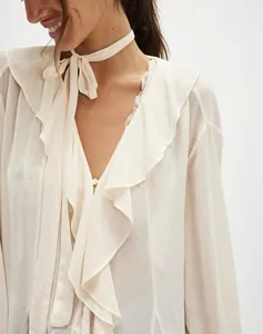 Primo piano di una camicetta di chiffon crema trasparente con volant e scollo a V