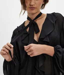 Dettaglio camicia nera trasparente in chiffon con scollo a V, volant e fiocco al collo.