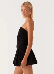Side view of elegant black strapless mini dress with pleated hem and gold knot earrings