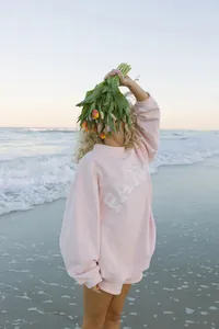 Detalle de una sudadera rosa de manga larga con letras FAN sobre fondo de playa soleada