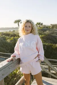 Foto de estilo de vida de mujer con conjunto de sudadera y pantalón corto rosa claro