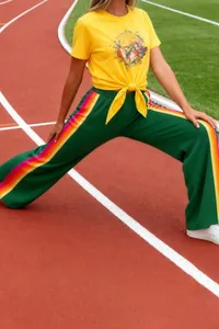 Detail view of women's green wide-leg pants with vibrant rainbow side stripes on track