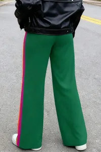 Detail view of women's green wide-leg pants with vibrant side stripes and black leather jacket