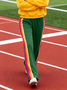 Women's green track pants with rainbow side stripes on a red running track