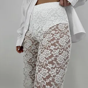 Detail of white high-waisted lace trousers featuring delicate floral sheer patterns