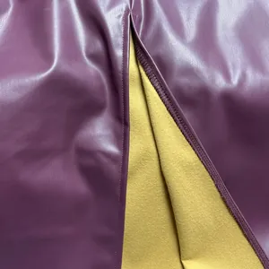 Detalle de una falda de cuero sintético púrpura con forro amarillo y bajo con abertura.