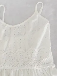 Detailaufnahme eines weißen Spitzenoberteils mit floraler Stickerei und Lochmustergewebe