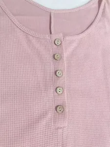 Primer plano de un mono rosa de punto gofrado con cuello abotonado y detalle de tela