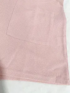 Primer plano de un mameluco rosa de punto gofrado con detalle de bolsillo y tejido