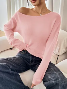 Detailed view of a pink knit sweater with a boat neck, styled with dark jeans on a model on a sofa.