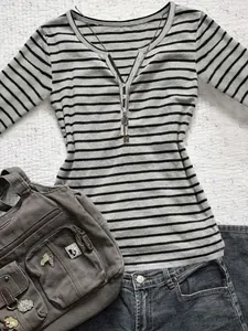 Detail view of a grey striped long-sleeve Henley T-shirt styled with a casual bag