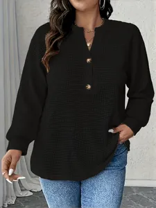 Detailansicht eines schwarzen Waffelstrick-Henley-Tops mit goldenen Knöpfen.