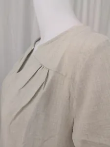 Close-up detail of a minimalist beige cotton linen dress neckline and pleated texture.