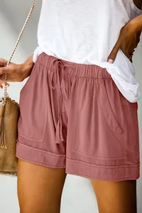 Dettaglio ravvicinato di pantaloncini rosa polvere a vita alta con coulisse e tasche.