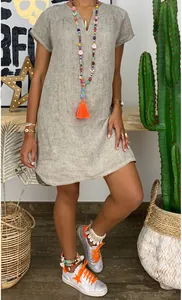 Detail view of a loose V-neck woven dress styled with boho beads and silver sneakers
