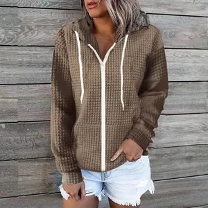 Detail view of a brown waffle-textured zip-up hoodie featuring white drawstrings and zipper